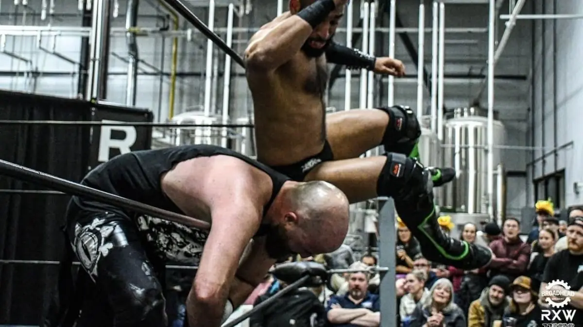 Tarik drops an elbow onto an opponent hung over the middle rope during a wrestling match.